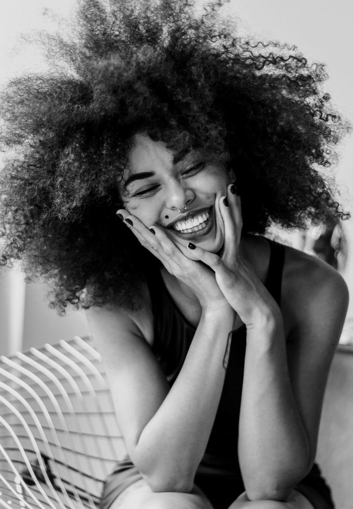 Retrato en blanco y negro de una mujer de pelo rizado que ríe con las manos en las mejillas